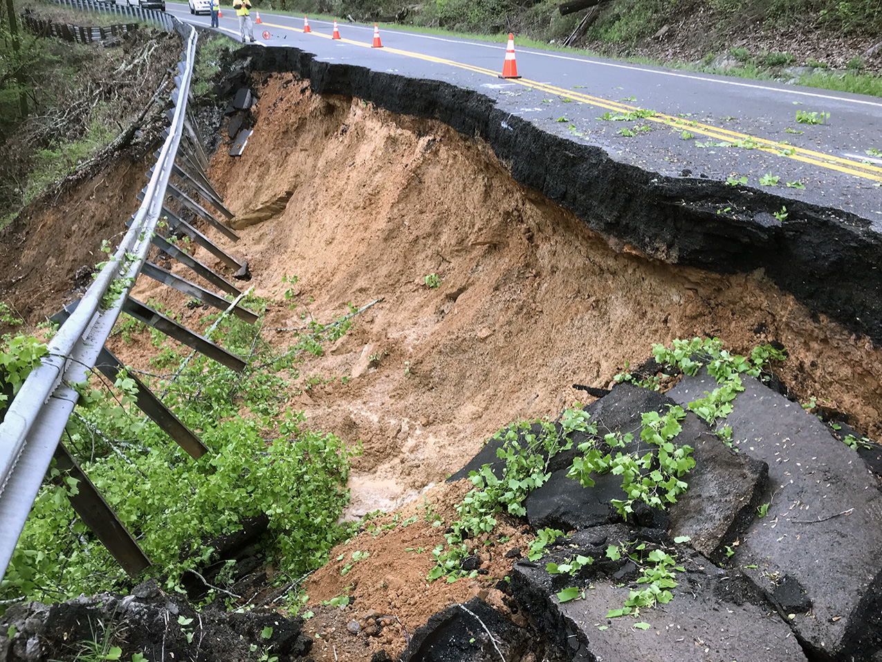 Roadway collapse due to landslide, with damaged pavement and exposed slope.