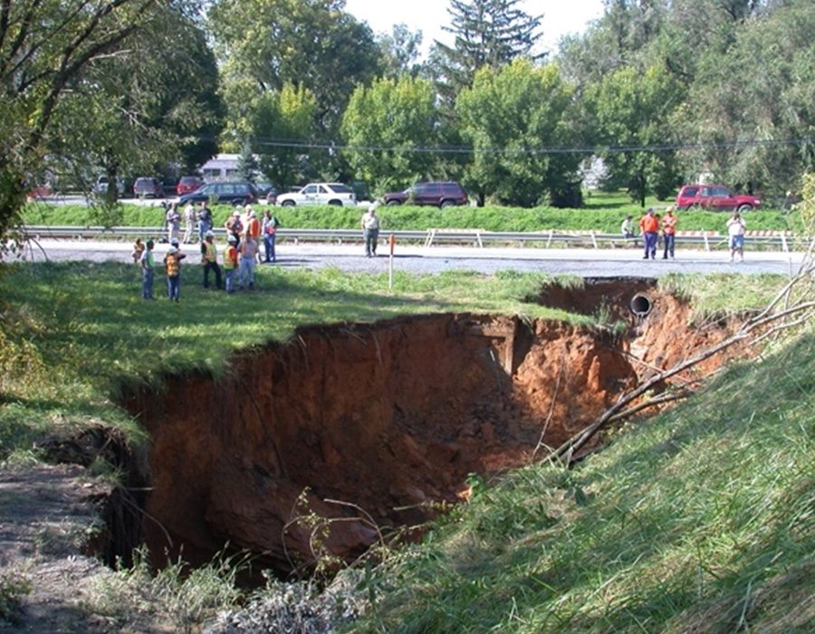 Large sinkhole near a road with people observing from a safe distance.