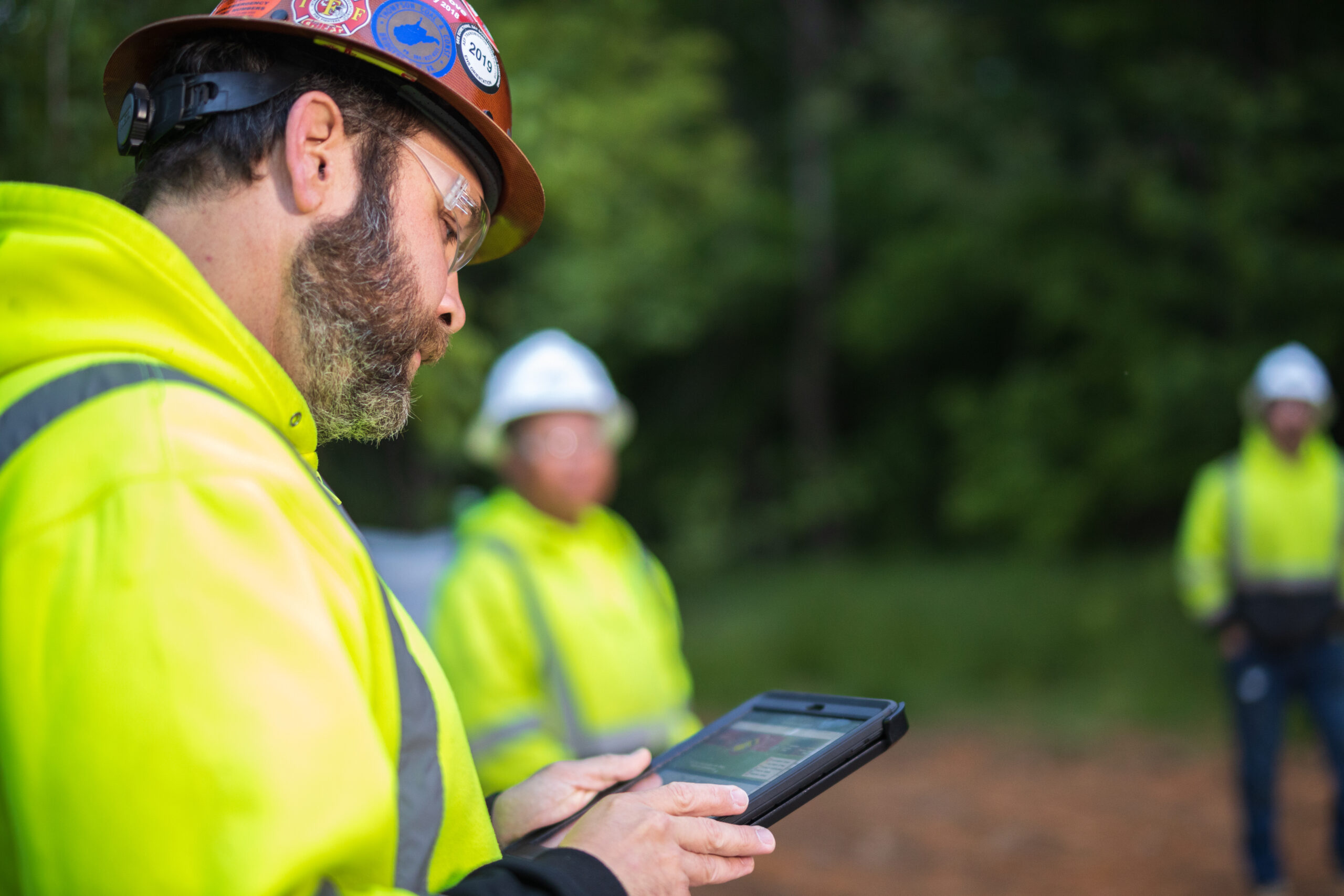 Construction worker in a hard hat and safety gear using a tablet.